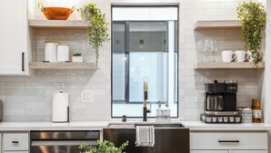 A modern kitchen with white cabinetry, a stainless steel range hood, a window with a view, and a coffee machine. - Comfortable Home in the Heart of West Seattle (Seattle)