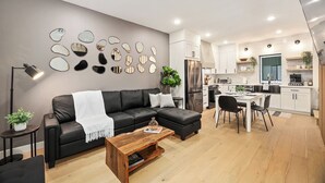 A modern living room with a black sofa, wooden coffee table, and a dining area with a white table and black chairs. - Comfortable Home in the Heart of West Seattle (Seattle)