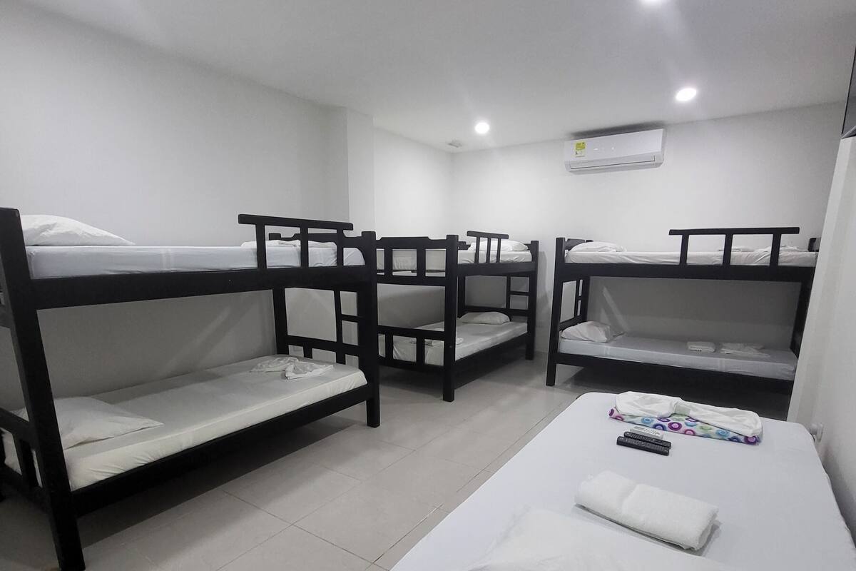 Ein Schlafsaalzimmer mit vier Etagenbetten, weißer Bettwäsche und einem Einzelbett mit Kissen und Handtuch.