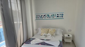 Un letto rifatto con cuscini bianchi e fantasia, un comodino con telecomando e una decorazione a parete sopra il letto.