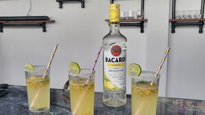 Un'area bar con tre bicchieri di cocktail al Bacardi, una bottiglia di Bacardi e scaffali con varie bottiglie e bicchieri.