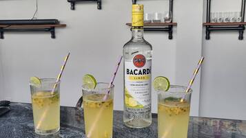 A bar area with three glasses of Bacardi rum cocktails, a bottle of Bacardi, and shelves with various bottles and glasses.