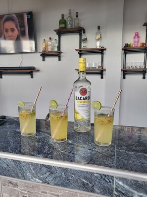 A bar area with three glasses of Bacardi rum cocktails, a bottle of Bacardi, and shelves with various bottles and glasses.