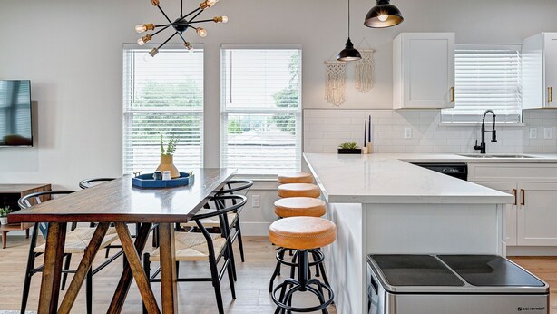 A modern kitchen with white cabinetry, a wooden dining table, and bar stools. - Modern HTX Apt: Free Wi-Fi, A/C, Full Kitchen, Free Parking (Houston)