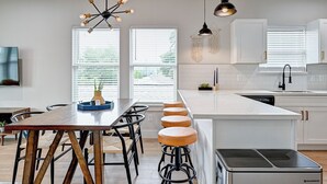 A modern kitchen with white cabinetry, a wooden dining table, and bar stools.