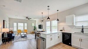 A modern kitchen with white cabinets, a dishwasher, and a dining area with a small table and chairs. - Modern HTX Apt: Free Wi-Fi, A/C, Full Kitchen, Free Parking (Houston)