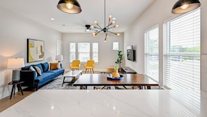 A modern living room with a blue sofa, yellow chairs, a wooden dining table, and a ceiling fan. - Modern HTX Apt: Free Wi-Fi, A/C, Full Kitchen, Free Parking (Houston)
