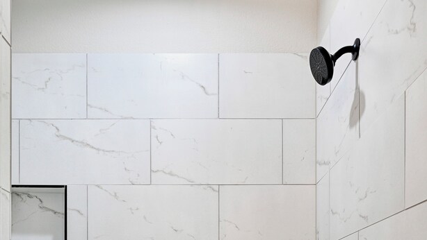 A shower with white marble tiles and a black showerhead.