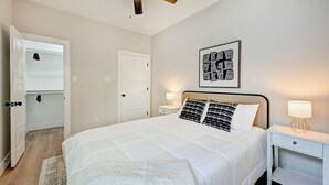 A bedroom with a bed, a nightstand, a ceiling fan, a door, and a wall-mounted picture. - Modern HTX Apt: Free Wi-Fi, A/C, Full Kitchen, Free Parking (Houston)