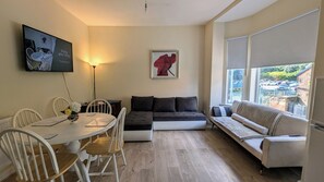 Un salon moderne avec une table à manger, un canapé et un divan. Il y a un tableau au mur et une lampe.