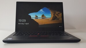Un ordinateur portable est posé sur une surface blanche. L’écran affiche une scène de plage, l’heure (19 h 09) et la date (lundi 1 er avril).