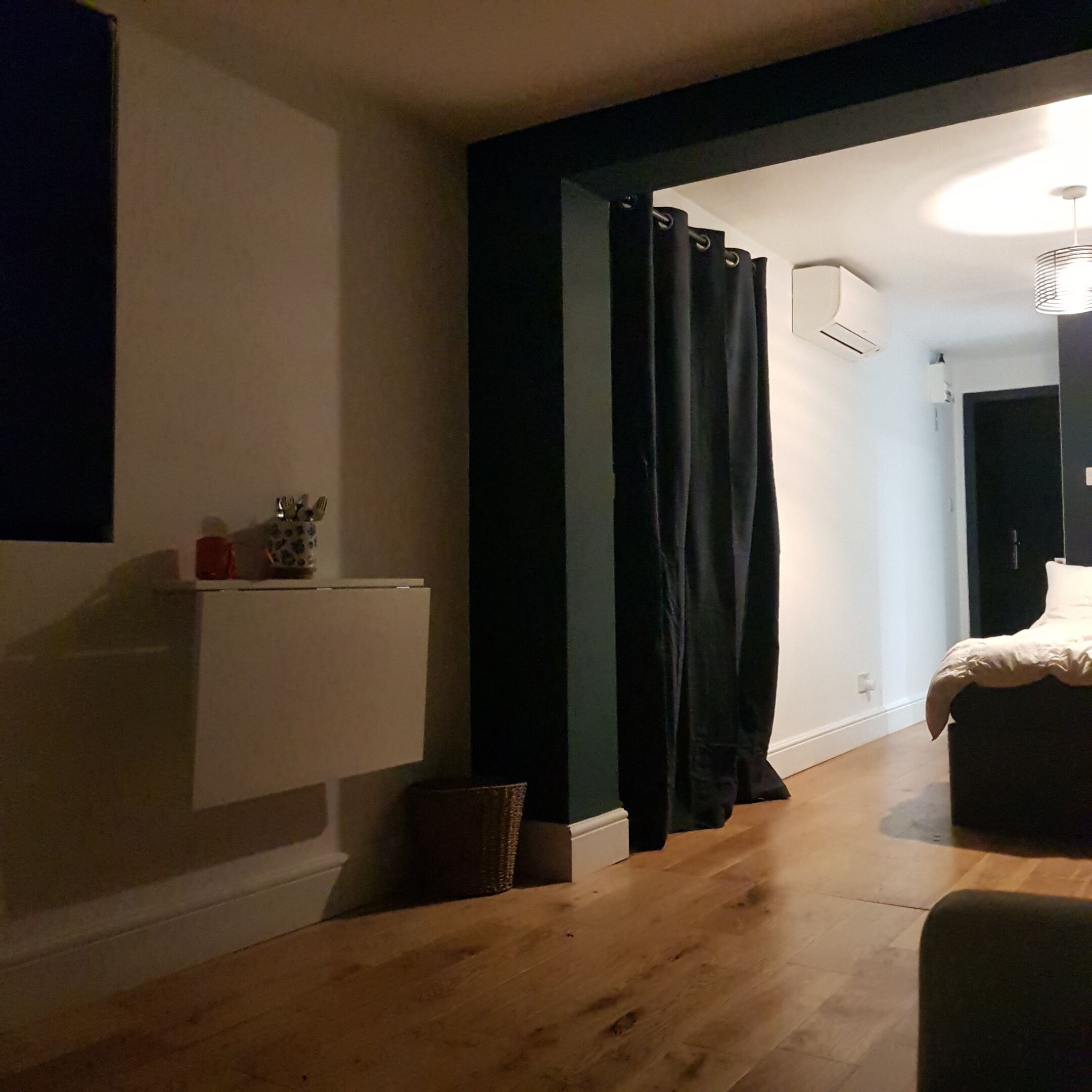 Une chambre à coucher avec un lit, un rideau foncé, une étagère avec divers objets et un plancher en bois.