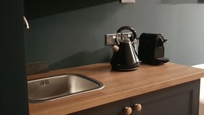 Une cuisine équipée d’un évier en acier inoxydable, d’une bouilloire et d’une machine à café posés sur le plan de travail.