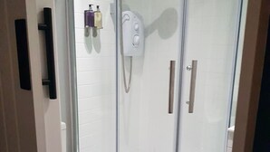 Une cabine de douche fermée par des parois en verre, avec des toilettes blanches sur la gauche.