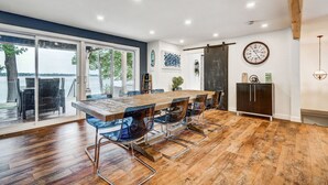 Een ruime eetruimte met een lange houten tafel en moderne stoelen, grote ramen met uitzicht, en een rustiek plafond.