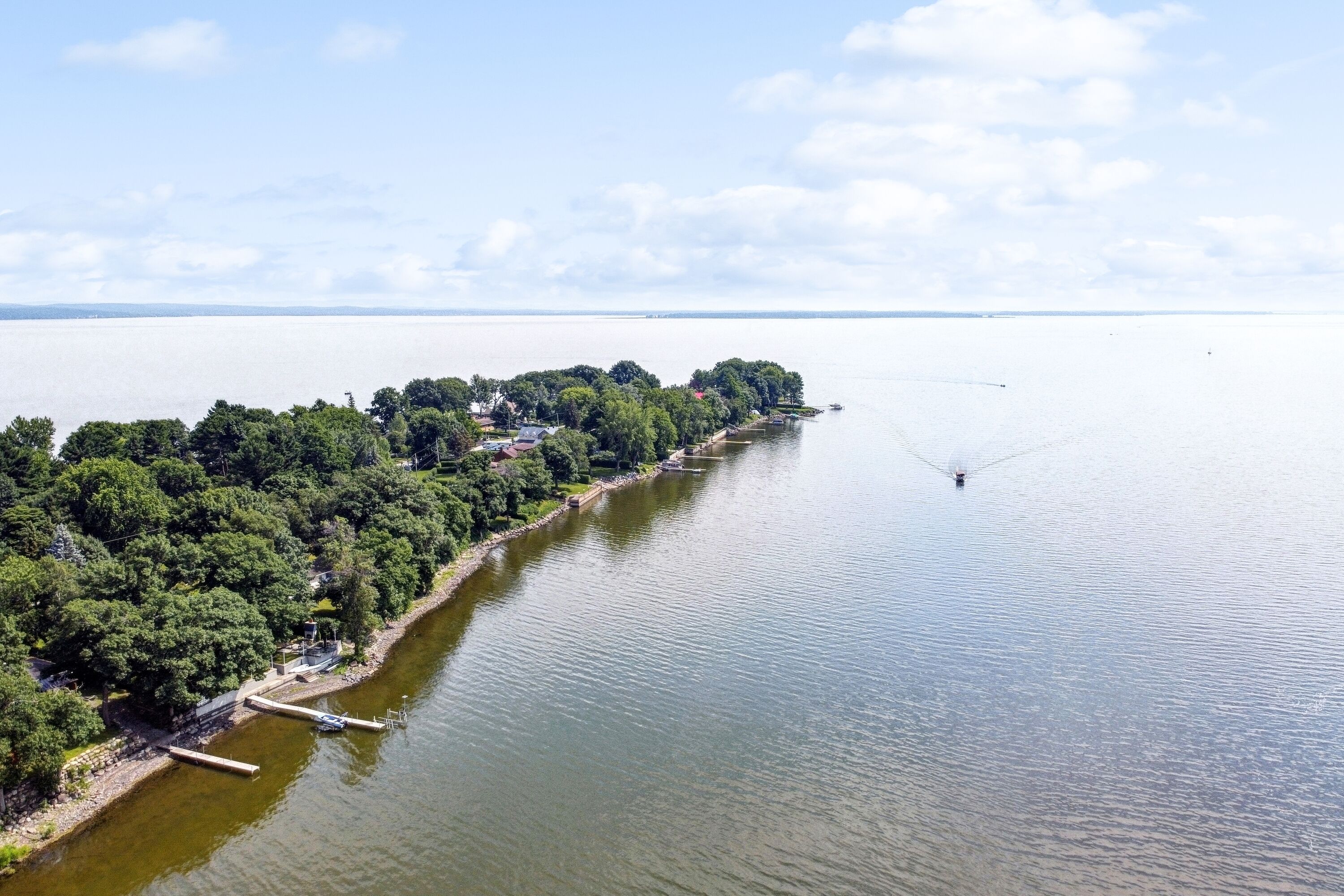 An aerial view of a lakeside property with a dock, trees, and a clear sky.