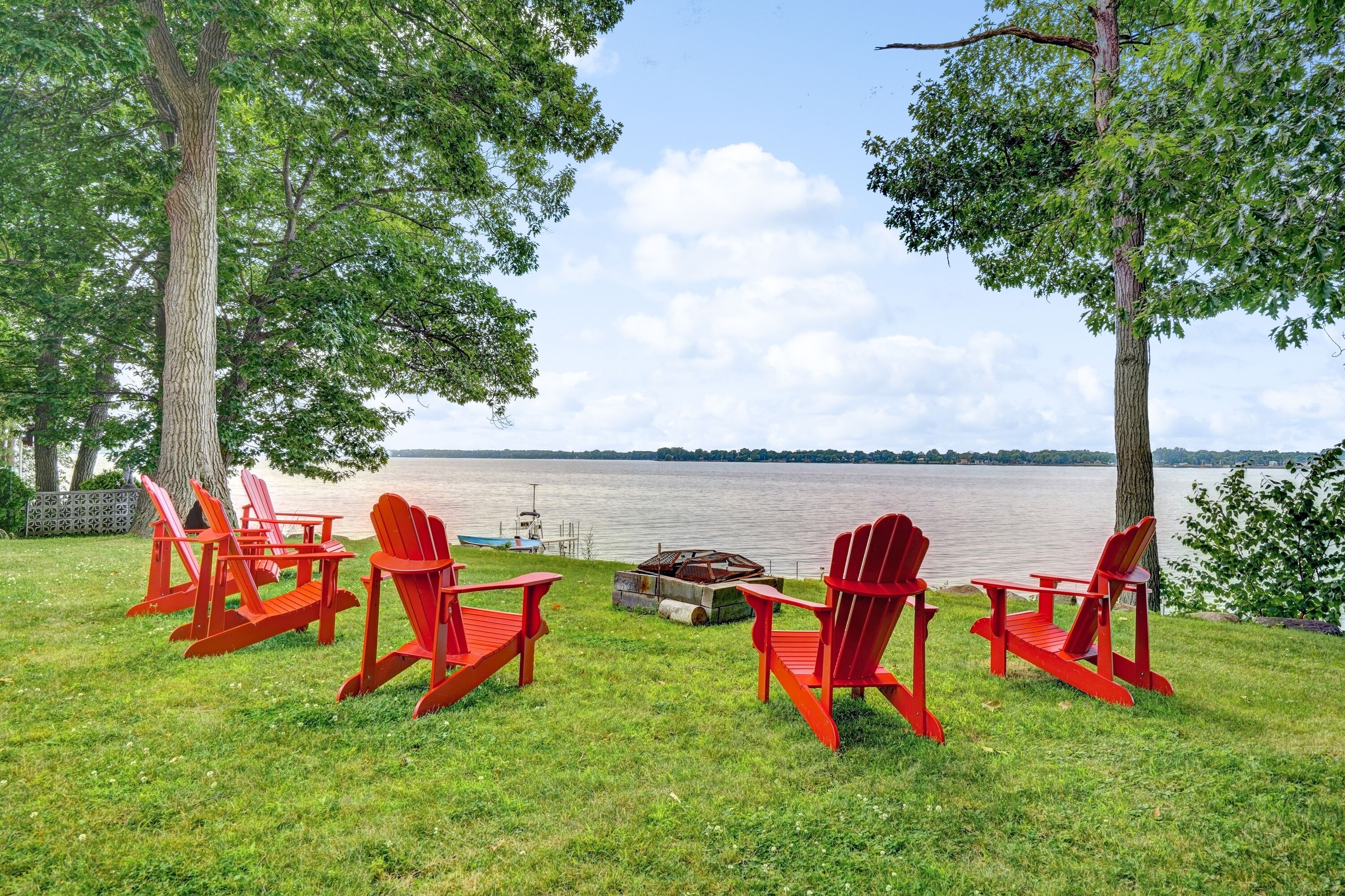 Un'ambientazione sul lago con poltrone Adirondack rosse disposte attorno a un braciere.