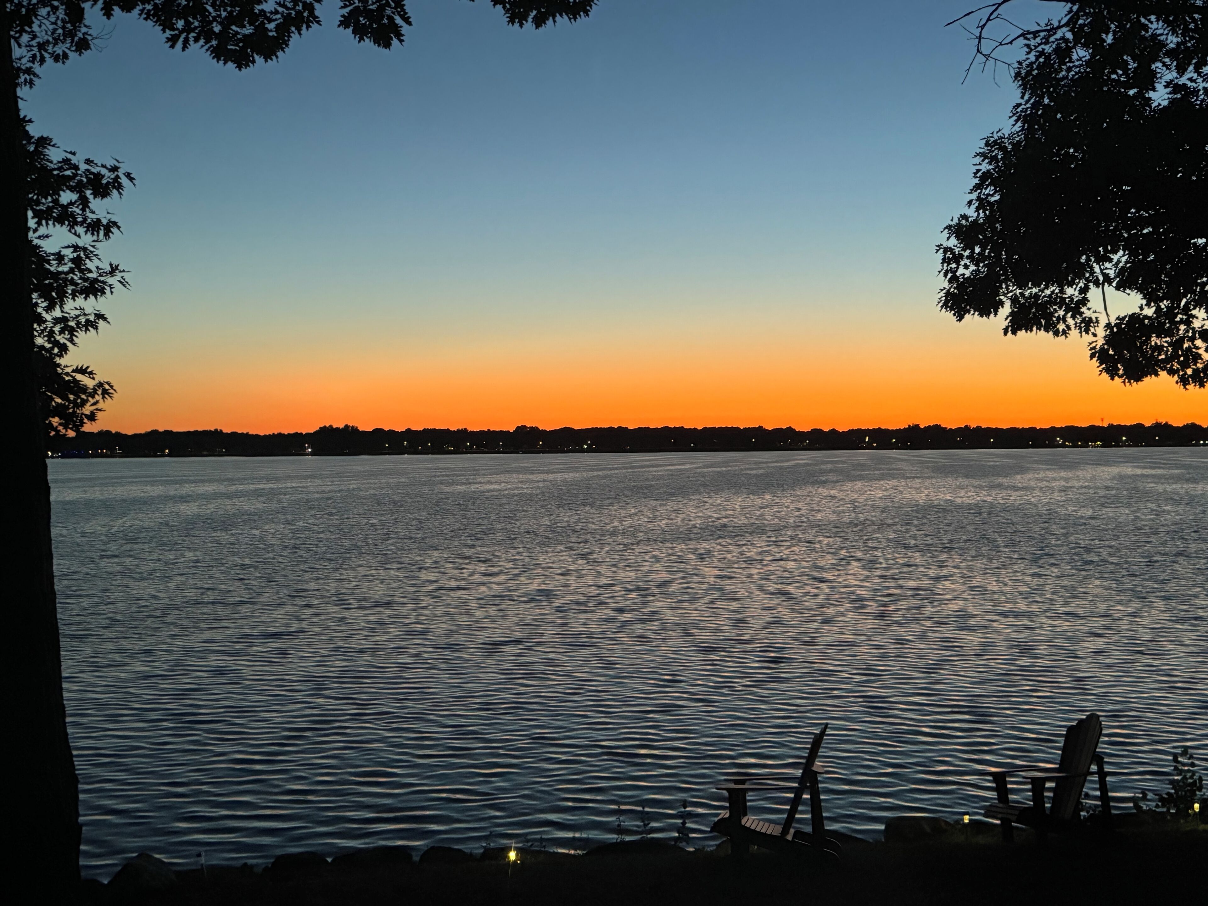 Une vue sur le lac au coucher du soleil, avec une eau calme et une chaise placée au bord de l’eau.