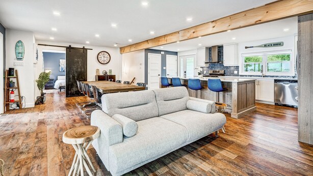 Een moderne keuken met houten balken, een eethoek met een grote tafel, en een woonkamer met een bank en salontafel.