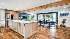 Een moderne keuken met houten kastjes, een groot eiland en een eethoek met uitzicht op de omgeving.