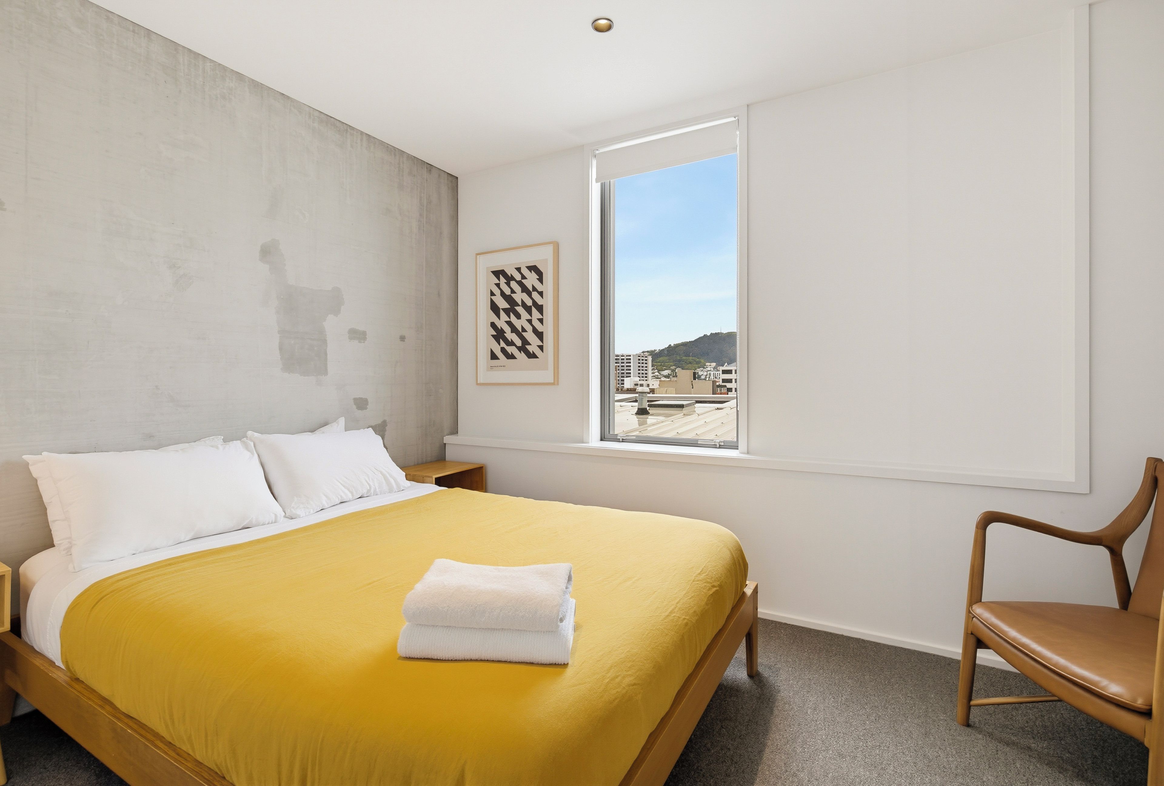 A hotel room with a bed, a window, a chair, and a framed picture on the wall.