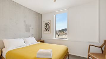 A hotel room with a bed, a window, a chair, and a framed picture on the wall.