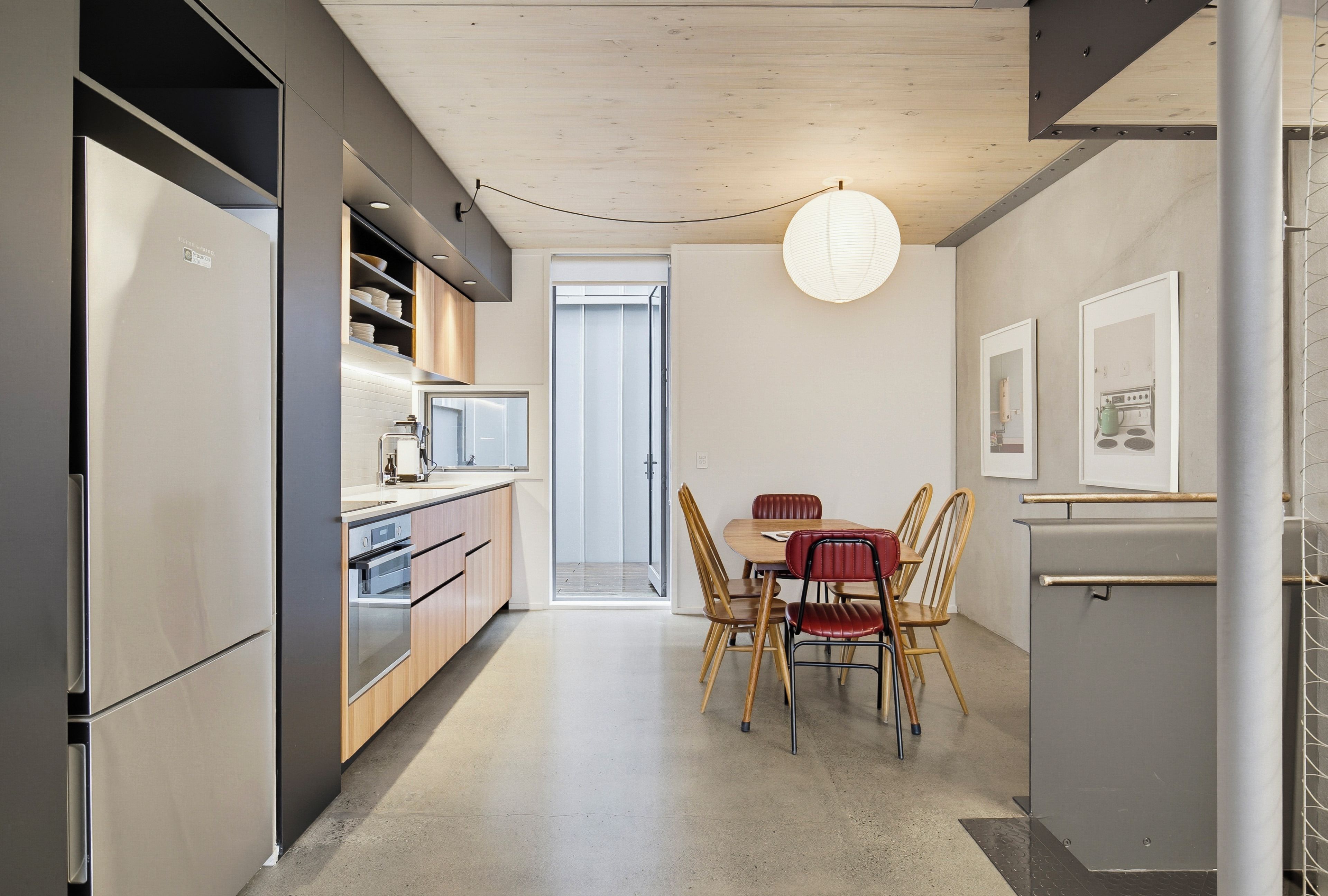 A modern kitchen with built-in appliances, a dining area with wooden chairs, and a pendant light.
