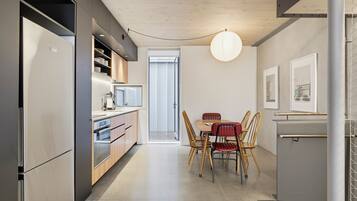 A modern kitchen with built-in appliances, a dining area with wooden chairs, and a pendant light.