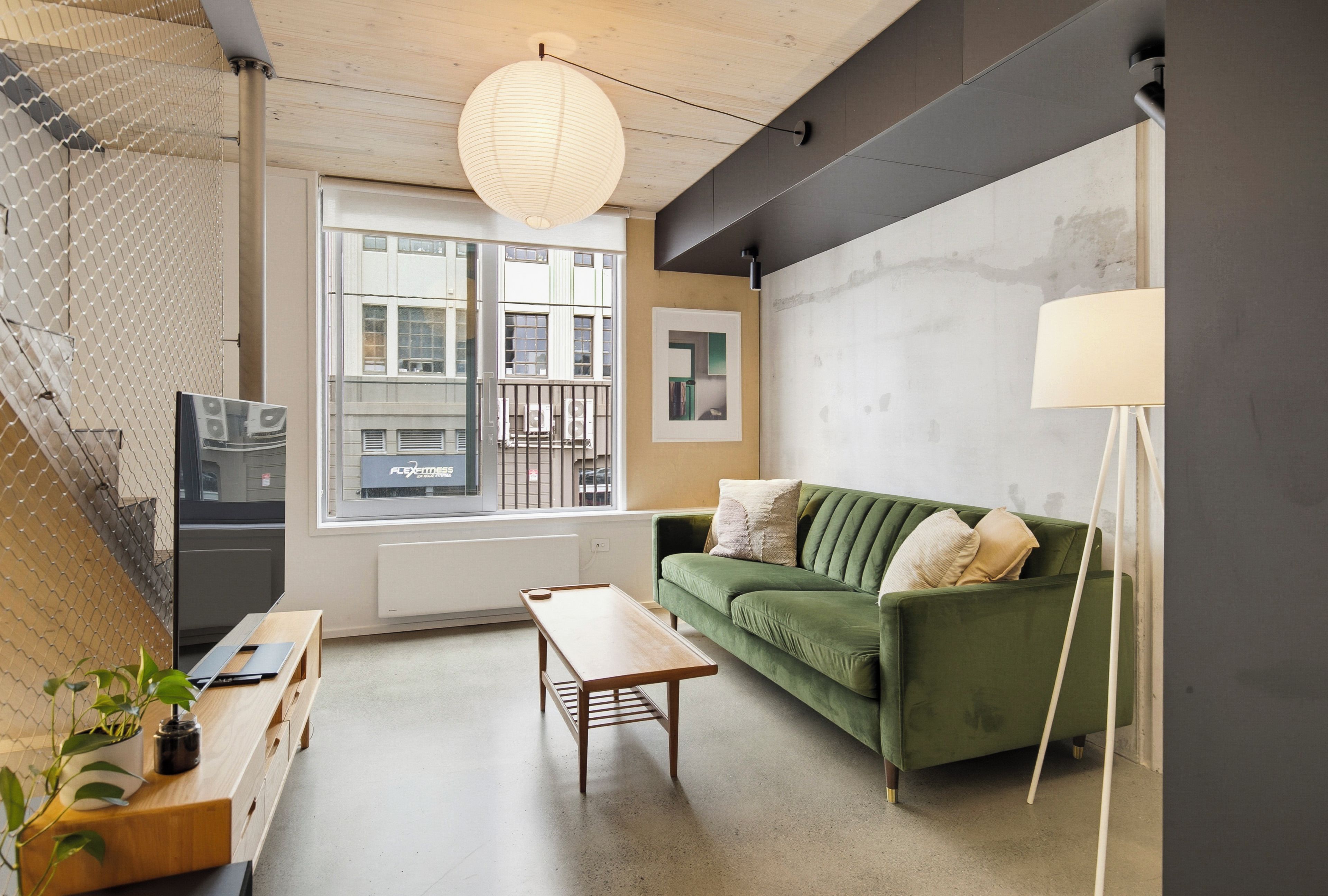 A modern living room with a green sofa, wooden coffee table, and a hanging light fixture.