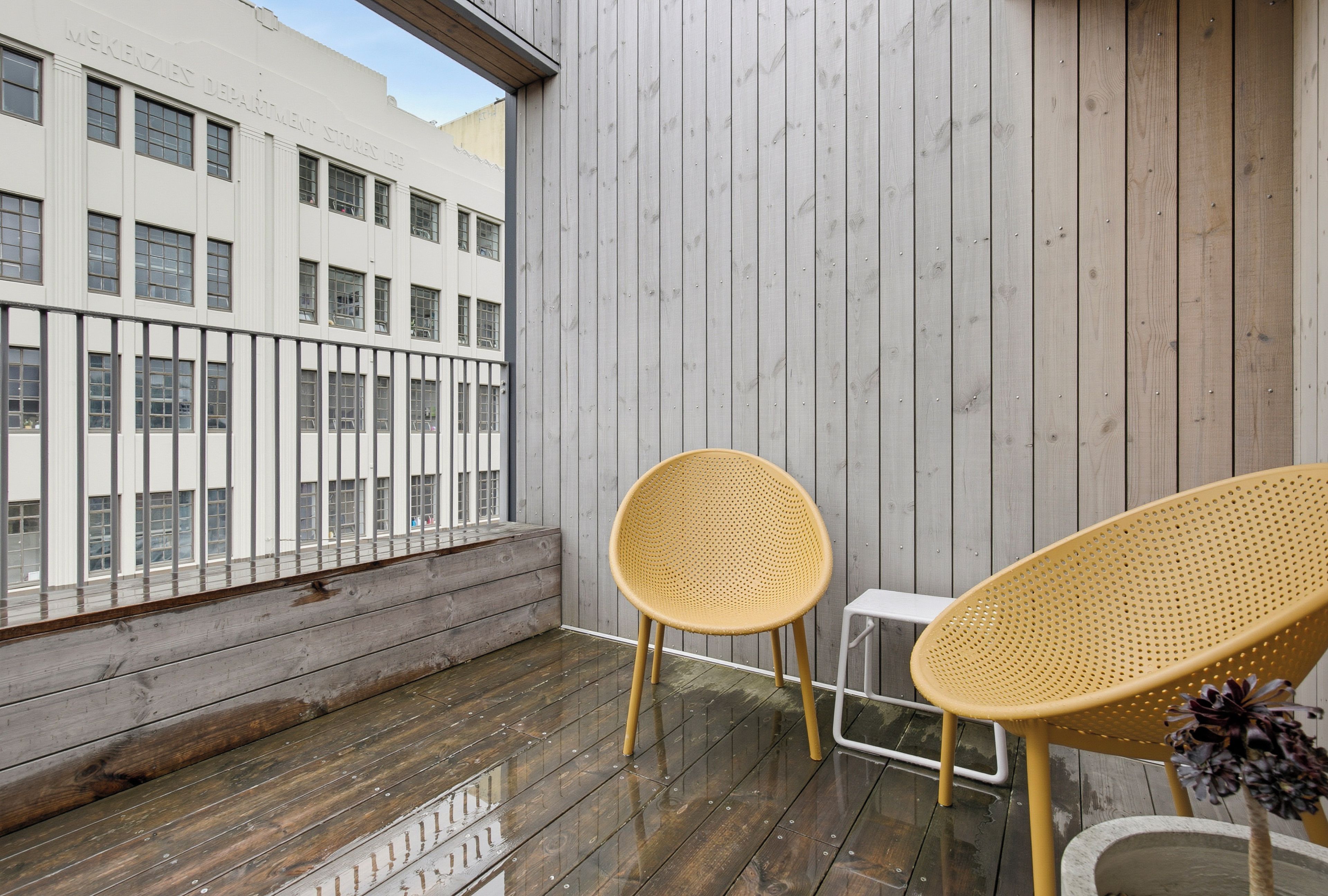 Ein Balkon mit zwei Korbstühlen und einem kleinen Tisch, mit Blick auf ein Gebäude mit vielen Fenstern.