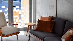 A modern living room with a grey sofa, a wooden armchair, and a small round table. - Luxury CBD townhouse 3 bed | 3 bath | 4 bed (Wellington)