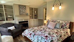 Ein Schlafzimmer mit Bett, einer Couch, einem Kamin, integrierten Regalen und einer Pendelleuchte.