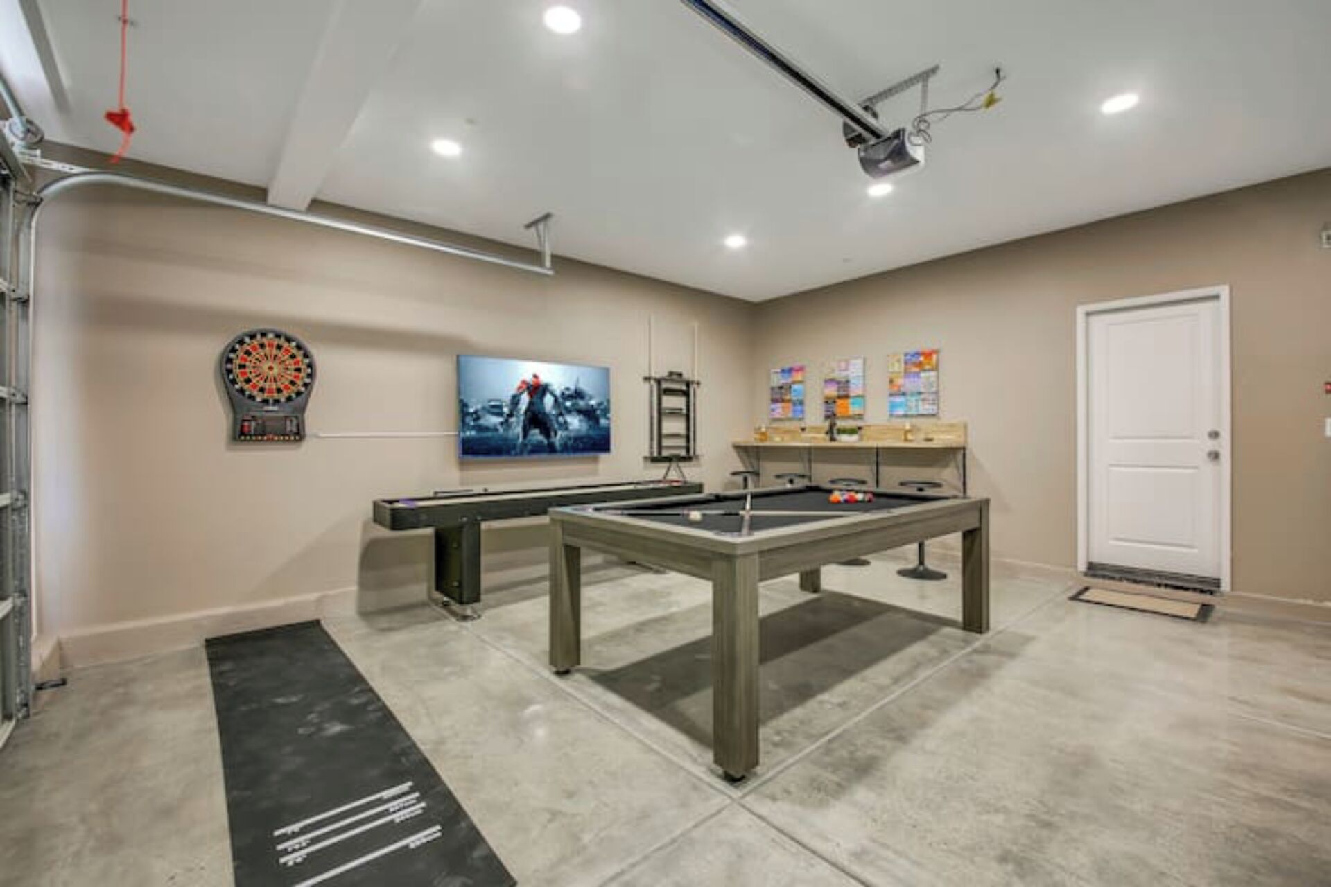 A pool table and dartboard in a room with a door, a dartboard, and a poster on the wall.