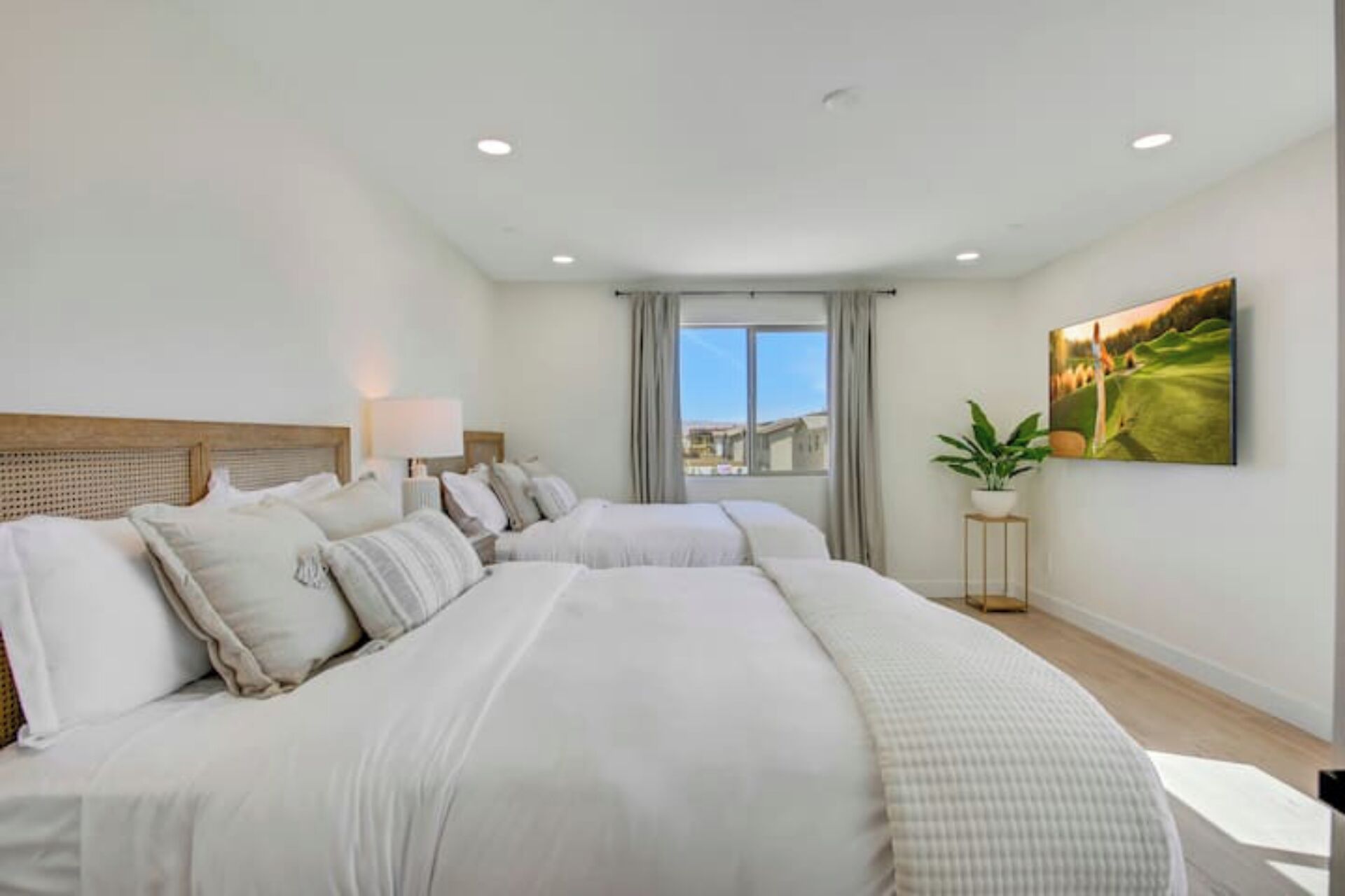 A hotel room with two large beds, a window with a view, a painting on the wall, and a small table with a plant.