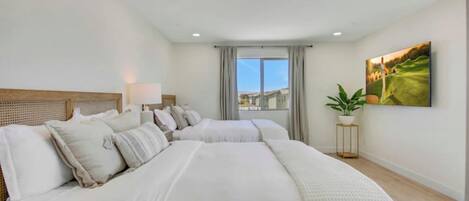 A hotel room with two large beds, a window with a view, a painting on the wall, and a small table with a plant.