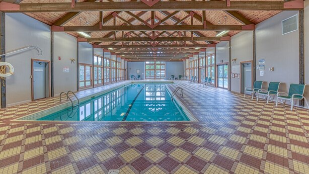Une piscine intérieure dotée d’un sol à carreaux, de poutres en bois et d’un plafond carrelé.