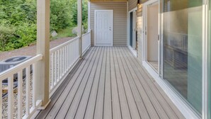 Une terrasse en bois avec une rambarde blanche, une porte et une porte-fenêtre coulissante.