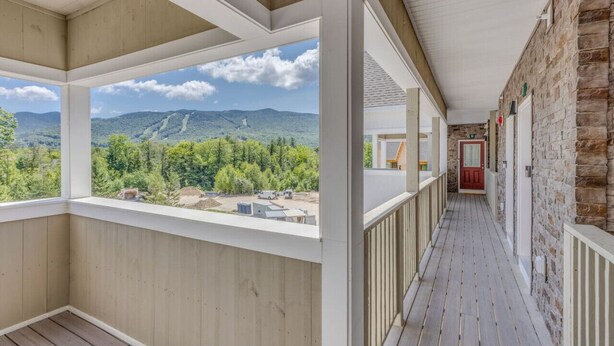 A covered porch with a view of mountains and trees, wooden flooring, and a stone wall. - Luxury Ski Condo- Forest Ridge (Lincoln)