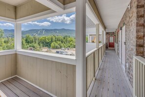 A covered porch with a view of mountains and trees, wooden flooring, and a stone wall. - Luxury Ski Condo- Forest Ridge (Lincoln)