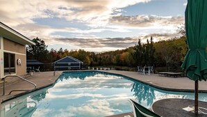 A swimming pool with a patio area, a covered seating area, and a building in the background. - Luxury Ski Condo- Forest Ridge (Lincoln)