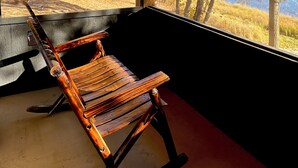 A wooden rocking chair facing a large window with a view of autumn trees.