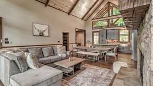 A spacious living room with a large sectional sofa, a dining table, and a kitchen area with stone countertops and wooden beams.