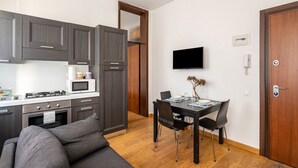 Una cocina compacta con electrodomésticos modernos, un comedor con mesa y sillas, y un televisor de pantalla plana montado en la pared.