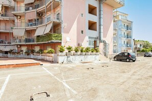 A multi-story residential building with balconies, a parking area, and a car parked in front.