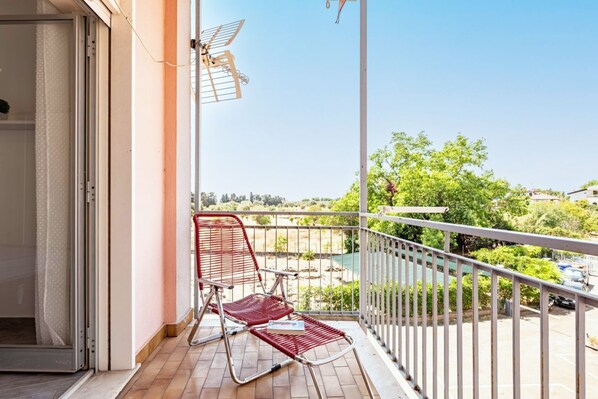 A balcony with a red chair, a white railing, and a view of greenery and buildings.