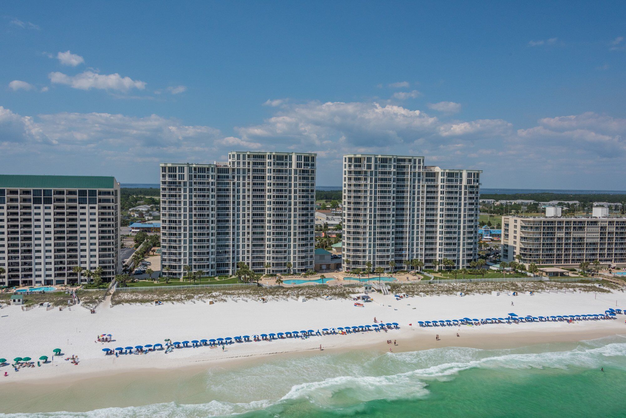 A beachfront hotel with multiple high-rise buildings, a sandy beach, and a clear view of the ocean.