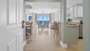 A spacious living area with a view of the ocean, a kitchen with modern appliances, and a dining area with wicker furniture. - Silver Beach Towers West 1105 | Destin | Beachfront, Outdoor Pool | My Beach Getaways (Destin)