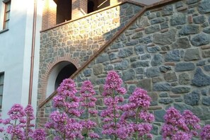 A stone building with a staircase and pink flowering plants in front.