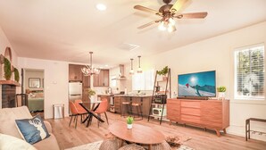 A modern living room with a sofa, coffee table, and a TV. There's a kitchen area with cabinets and a dining table. - Cozy Modern Cabin Near Lake, Spa, Village, & Ski Slope (Big Bear Lake)