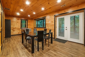 A wooden-paneled room with a glass-top dining table and chairs, a door with a window, and a door with a window.